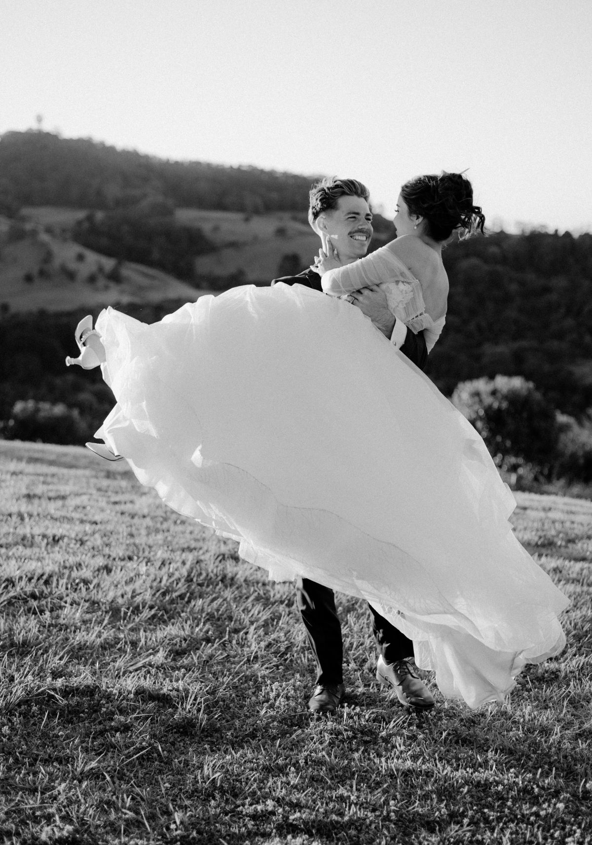 Groom swings bride around romantically on top of the rolling hills of the Tweed Coast